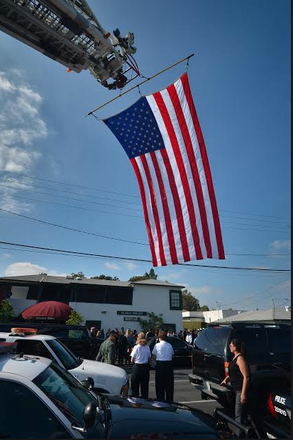 A flag flies from a fire department ladder as the body of Lt. Ken Alexander of the Placentia Police Department, who died of a heart attack, is taken to the McAulay & Wallace Mortuary in Fullerton. Photo by Steven Georges/Behind the Badge OC