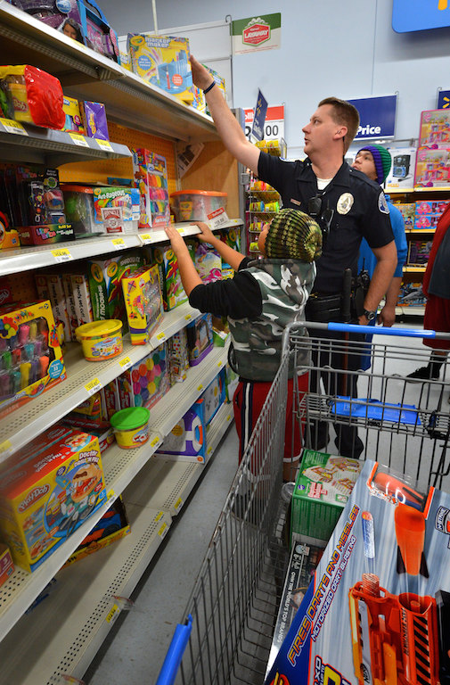 Westminster Police Officer Travis Hartman helps Jonathan Rodriguez, 10 of Westminster, reach a toy on the top shelf during their Shop with a Cop shopping spree at Walmart. Photo by Steven Georges/Behind the Badge OC