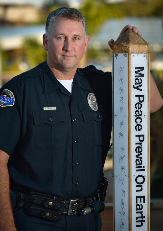 Motor Officer Mark Van Meter of the Huntington Beach Police Department stands next to a good will post in front of the Huntington Beach Civic Center written in multiple languages including sign language. Photo by Steven Georges/Behind the Badge OC