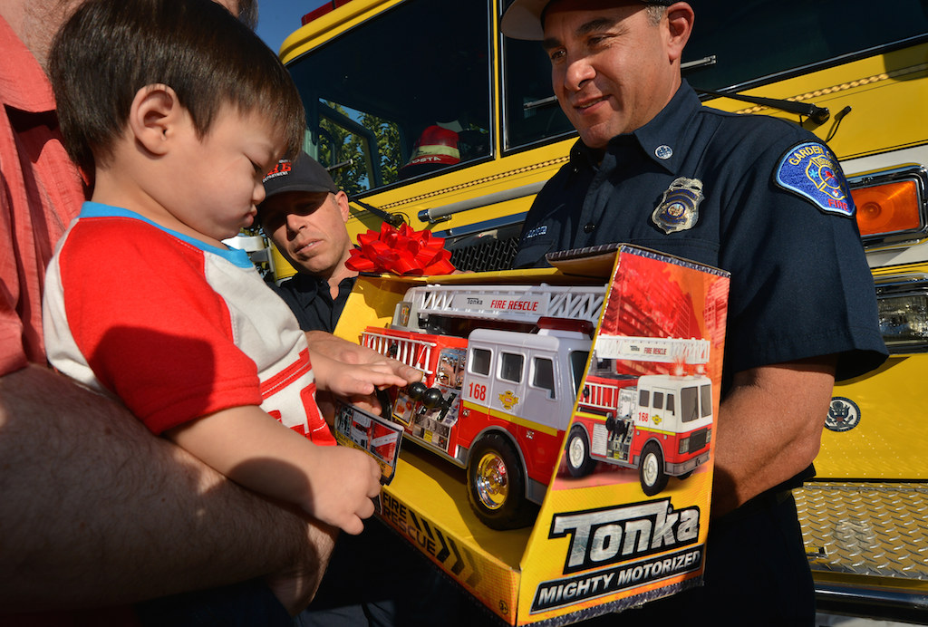 Caleb receives a fire engine from Paramedic Ryan Van Wie and Fire Captain Tony Acosta.  Photo by Steven Georges/Behind the Badge OC