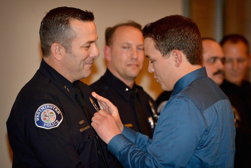 Deputy Chief Dan Schoonmaker of the Westminster PD gets his new badge pinned on him by his son during a promotion ceremony at the Rose Center in Westminster. Photo by Steven Georges/Behind the Badge OC