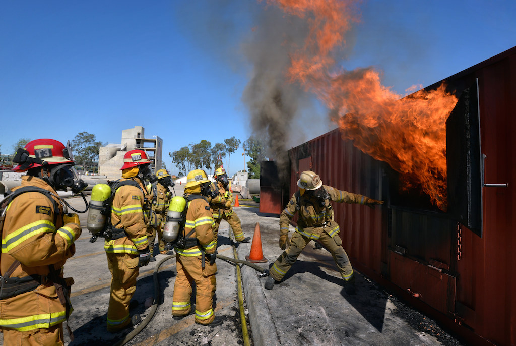 Battalion Chief Tim Adams, right, shows firefighters how quickly flames from a fire can erupt after it is given oxygen from an opening during a training fire set inside a customized shipping container at the North Net Fire Training center in Anaheim. Photo by Steven Georges/Behind the Badge OC