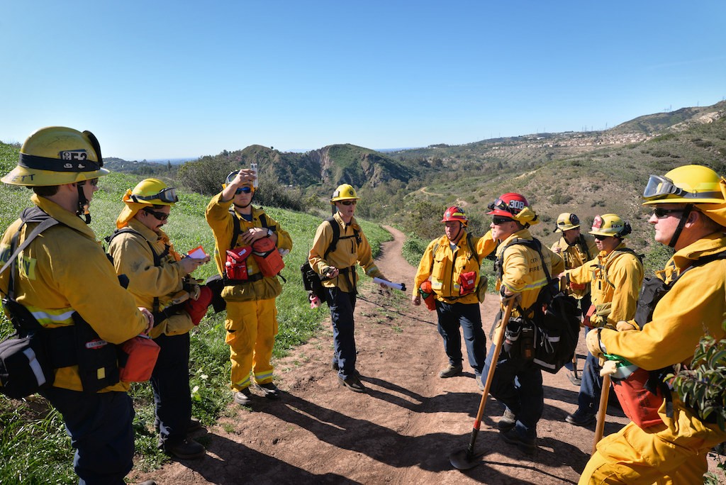 Firefighter James Moreta, forth from left, and Captain Jerry George, sixth from left, of Anaheim Fire & Rescue go over procedures, including obtaining temperature, humidity, and wind readings from portable devices that can be radioed back to command posts, during a wildfire training session at Santiago Oaks Regional Park. Photo by Steven Georges/Behind the Badge OC