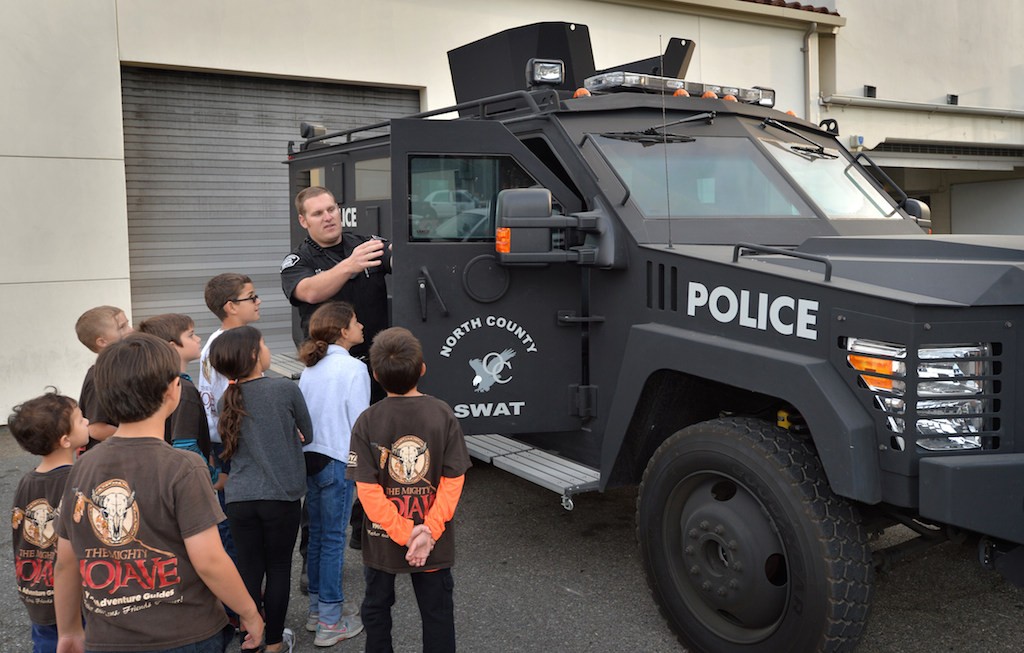 Officer Jonathan Miller of the Fullerton PD gives kids from YMCA Adventure Guides a tour of a North County armored SWAT truck during a visit to the Fullerton Police Department. Photo by Steven Georges/Behind the Badge OC
