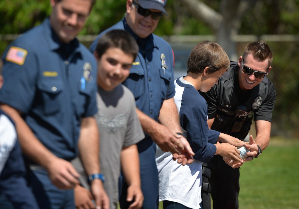 Officer Andrew Coyle of the Fullerton PD, right, helps in a during a demonstration relay with cans of food as Fullerton Police and Fire Departments visit Rolling Hills Elementary School for a Team Kids assembly. Photo by Steven Georges/Behind the Badge OC