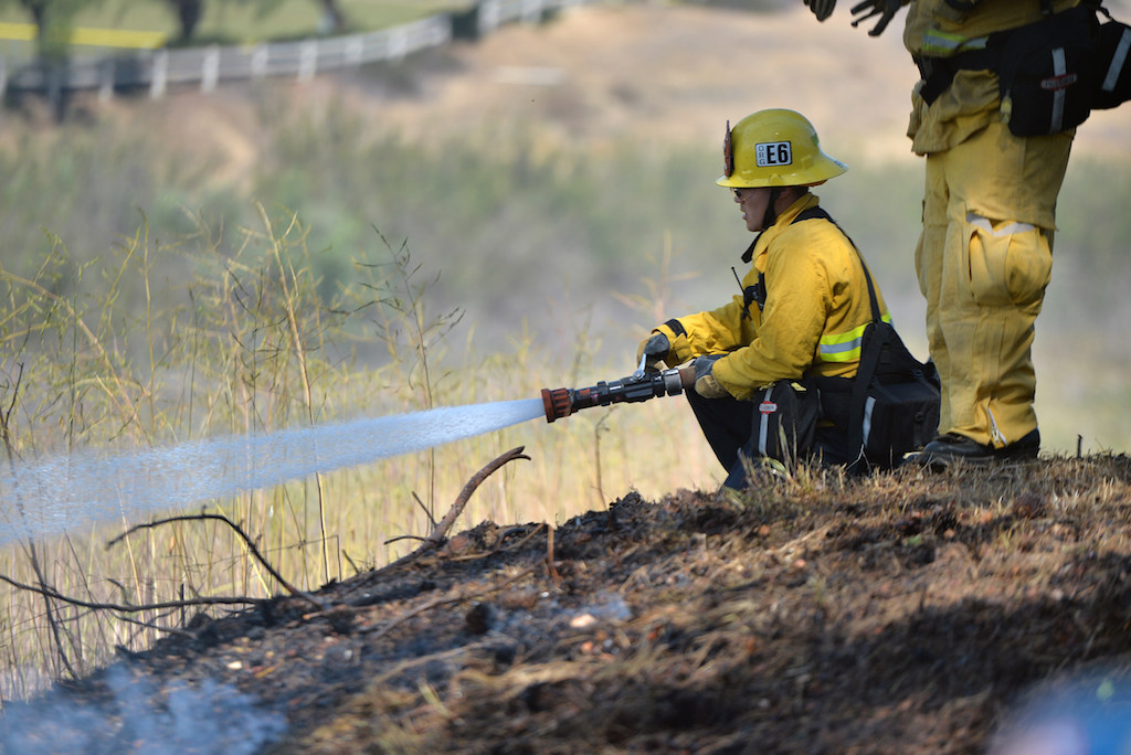 A firefighter from the City of Orange Fire Department sprays water on the local brush as a vegetation fire that broke out in the Brea Dam Recreation Area Saturday afternoon threatening homes in the area. Photo by Steven Georges/Behind the Badge OC