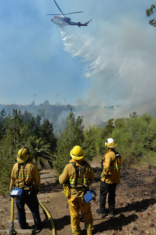 Anaheim Firefighters Gamble, left, Anthony Manzo and Battalion Chief Jeff Thomas watch a helicopter from Orange County Fire Authority drop water on a vegetation fire that broke out in the Brea Dam Recreation Area Saturday afternoon. Photo by Steven Georges/Behind the Badge OC
