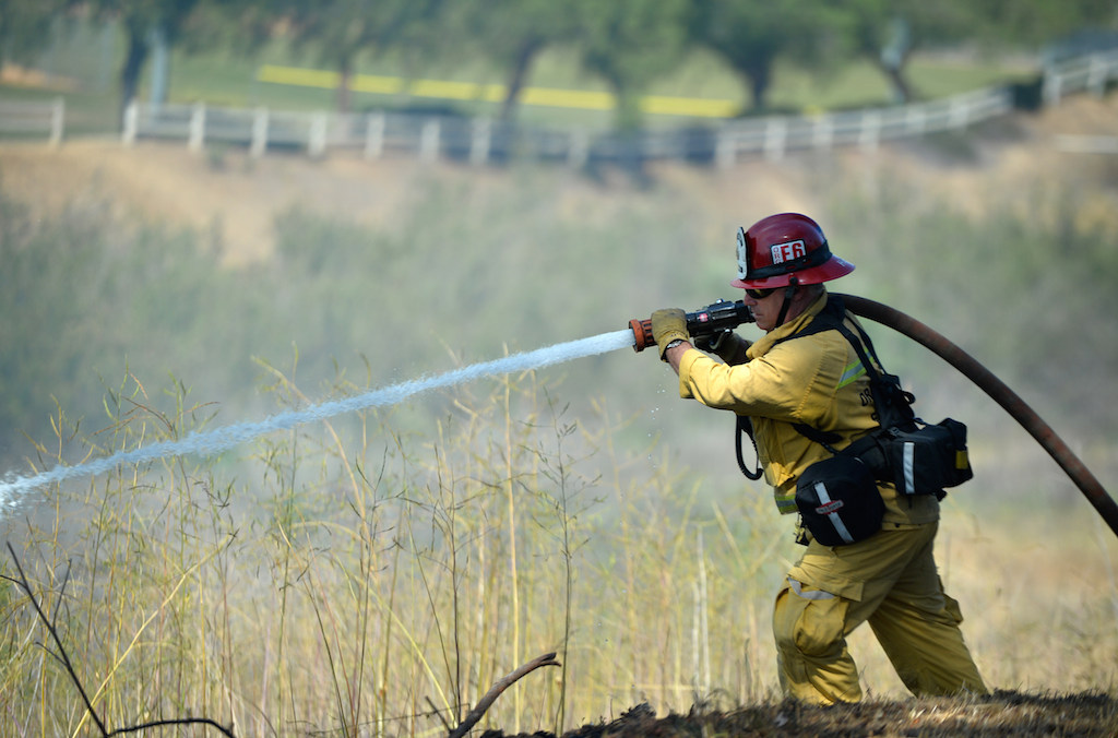 Captain Hoff of the City of Orange Fire Department sprays water on the local brush as a vegetation fire that broke out in the Brea Dam Recreation Area Saturday afternoon threatening homes in the area. Photo by Steven Georges/Behind the Badge OC