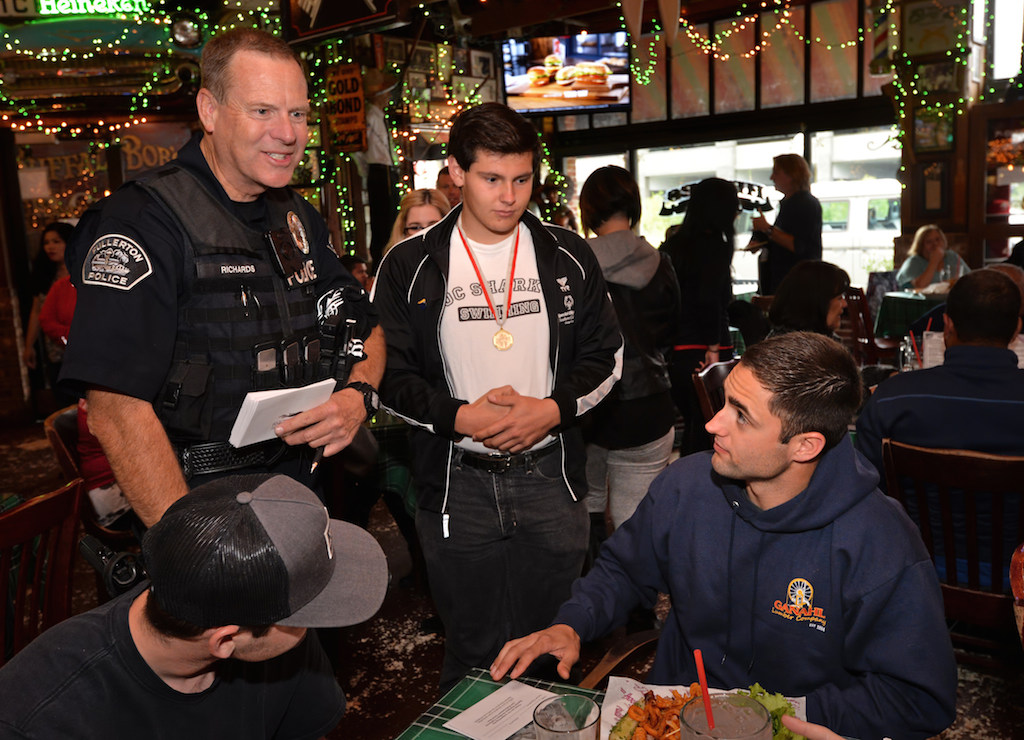 *** (Randall Richards?) *** Officer Richards of Fullerton PD walks up to tables at Heroes Bar and Grill in Fullerton with Christian Valdez, last year’s Special Olympics gold medal Athlete in the butterfly, telling guest about the Tip-A-Cop fundraiser benefiting the Athletes of Special Olympics Orange County. Photo by Steven Georges/Behind the Badge OC