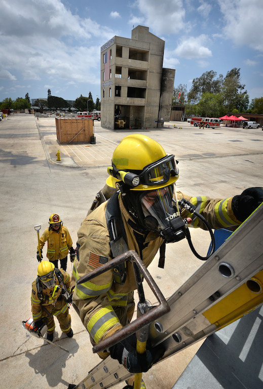 Recruit Carlos Torres climes to the roof of a training building to cut a hole in the roof, in order to vent heat so firefighters can enter the building, during a training exercise at the North Net Training center in Anaheim Photo by Steven Georges/Behind the Badge OC