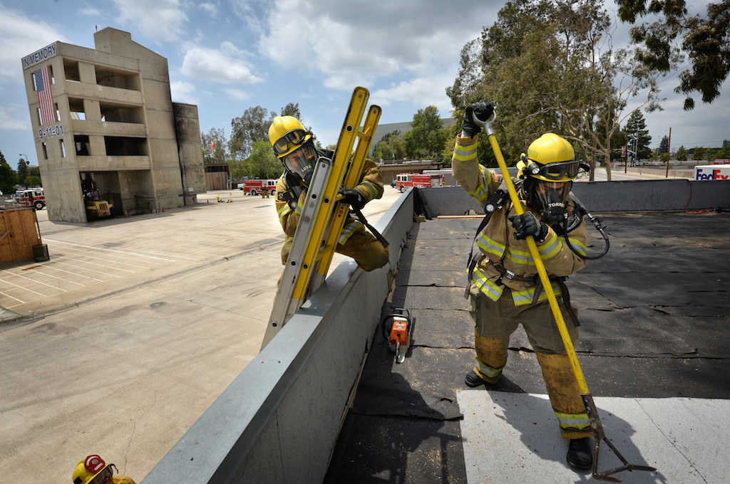 Recruit Carlos Torres, right, test the stability of each section of roof he plans on walking on as David Loya follows on the ladder during a training exercise at the North Net Training center in Anaheim. Photo by Steven Georges/Behind the Badge OC