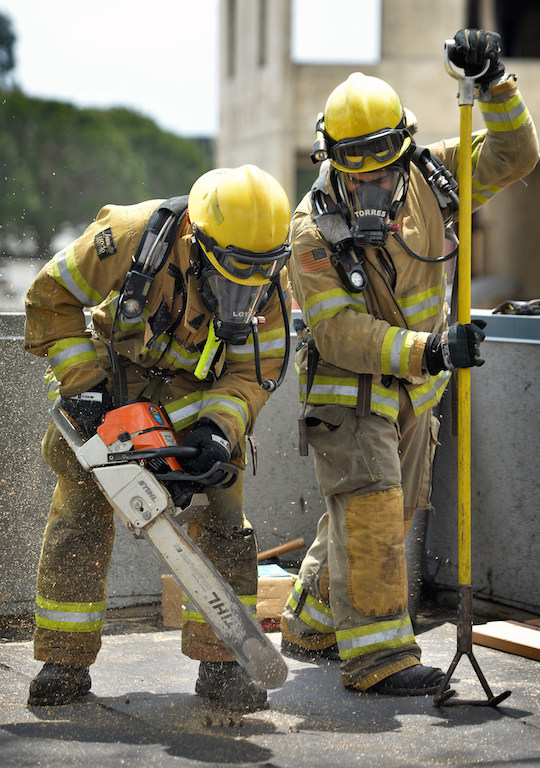 Recruits David Loya, left, and Carlos Torres cut a hole in the roof, in order to vent heat so firefighters can enter the building, during a training exercise at the North Net Training center in Anaheim. Photo by Steven Georges/Behind the Badge OC