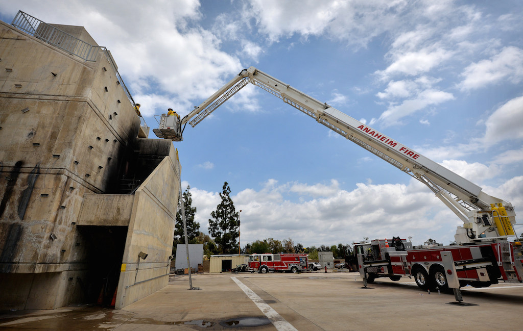 The ladder from Anaheim Fire & Rescue Truck 3 carries recruits to the North Net Training Center tower during a training exercise. With the support braces in place, all ten wheels of the truck are lifted off the ground. Photo by Steven Georges/Behind the Badge OC