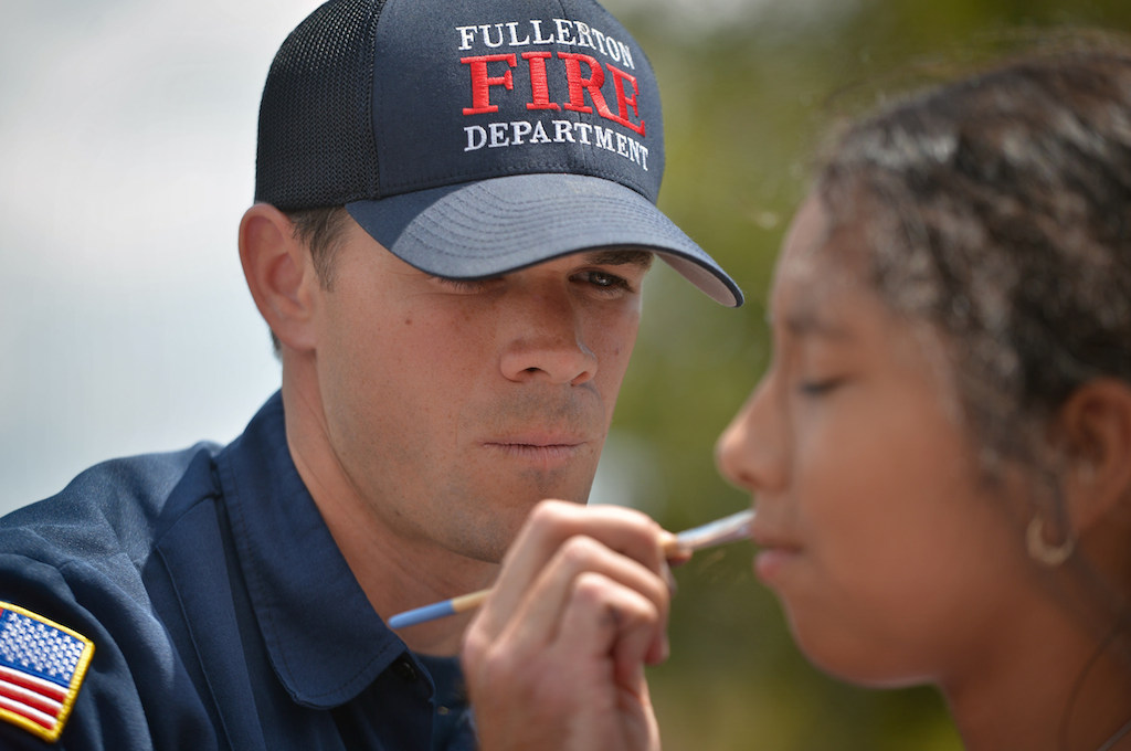 Fullerton Firefighter David Brown paints a cupcake on 10-year-old Klarissa Aguero during the Team Kids Challenge Carnival at Rolling Hills Elementary in Fullerton benefiting cystic fibrosis research and education. Photo by Steven Georges/Behind the Badge OC