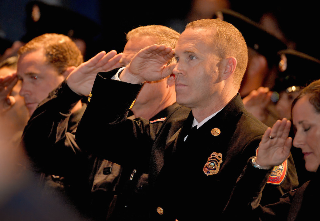 Firefighters salute during the singing of the national anthem at the start of the Anaheim Fire & Rescue Promotion and Graduation ceremony at The Grove. Photo by Steven Georges/Behind the Badge OC