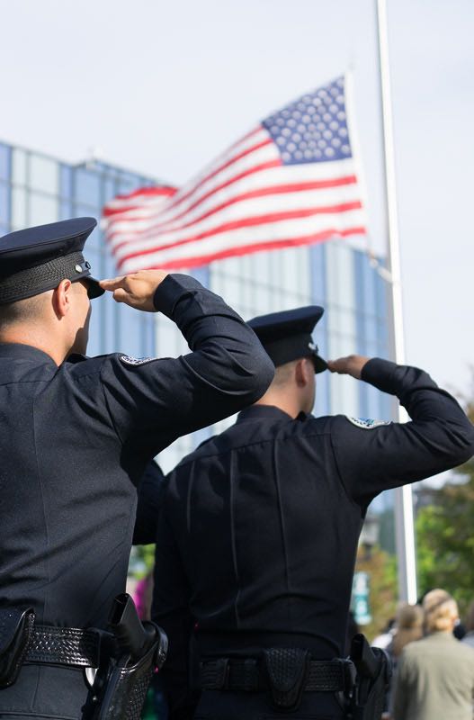 Uniformed personnel salute as the American flag is raised to half-mast to honor those killed in the line of duty. Photo by Jim Banks/Behind the Badge OC. 