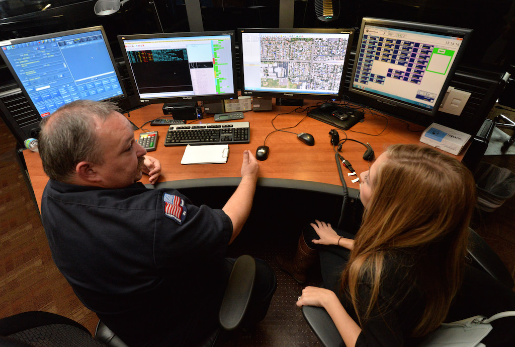 Mike Bates, lead dispatcher with Metro Cities Fire Authority gives a 911 station orientation to Allie Kuramata, 24, of Rancho Cucamunja at the Metro Cities 911 dispatch center in Anaheim. Photo by Steven Georges/Behind the Badge OC