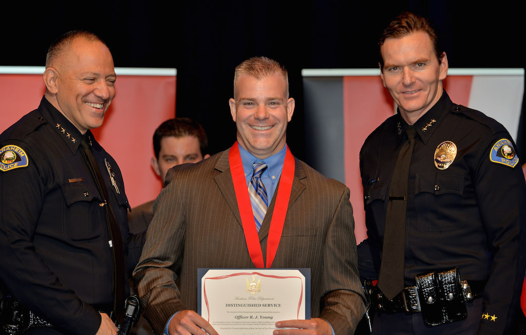 Officer R.J. Young, center, receives the Distinguished Service medal for “courageous and brave actions while providing emergency assistance while shot were fired on partners at the Orange County Probation Department”, from Anaheim Police Chief Raul Quezada, left, and Deputy Chief Julian Harvey during Anaheim PD’s 2015 Awards and Retirement Ceremony. Photo by Steven Georges/Behind the Badge OC