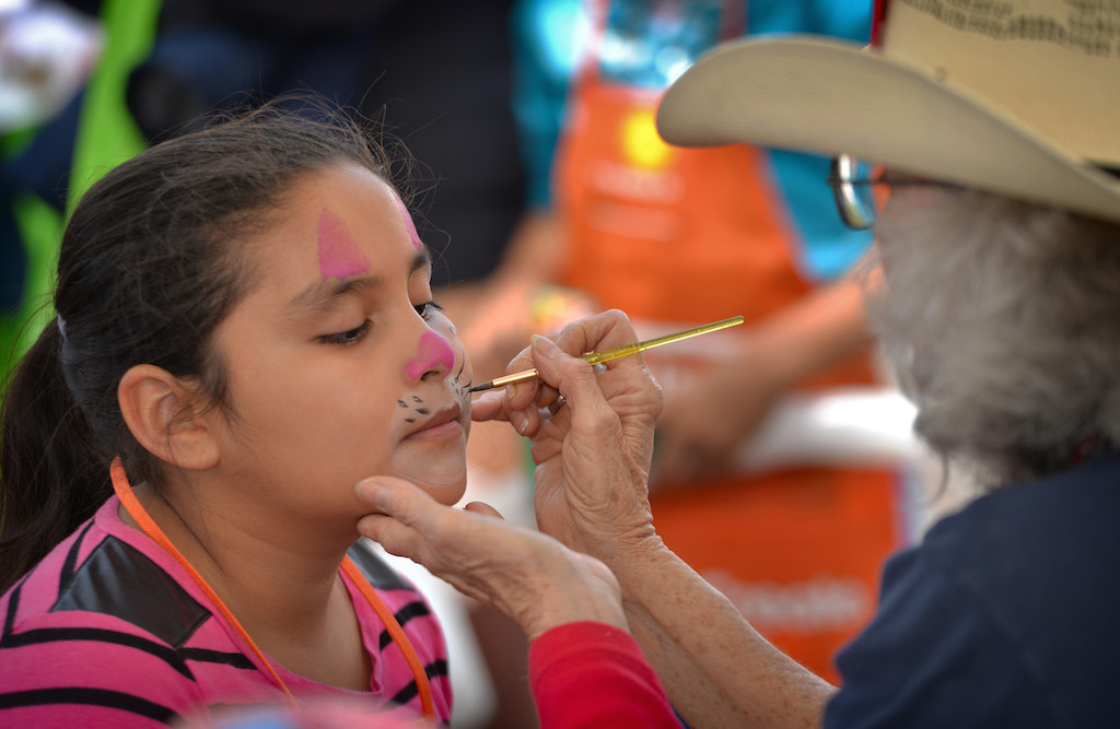 Eight-year-old Citlaly Palma gets her face painted by “Silly Tilly” (Carla Tillia of Huntington Beach), of Volunteer Clowns of Orange County, during a neighborhood cleanup and community gathering along Laguna Street in Garden Grove. Photo by Steven Georges/Behind the Badge OC