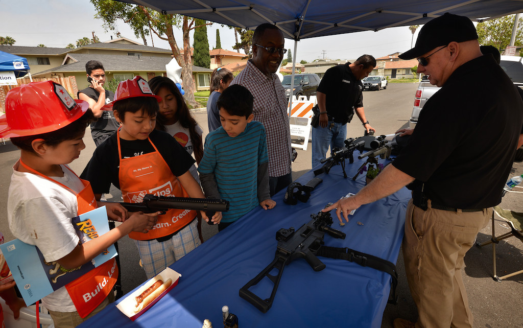 White Eison Alonzo, 10, left, Julio Garcia, 9, and Kevin Lopez, 11, look over the (unloaded) weapons and other tools, that Garden Grove police officers train with, under the watchful guidance of Sgt. (Michael?*) Martin, right, during a neighborhood cleanup and community gathering along Laguna Street in Garden Grove. Photo by Steven Georges/Behind the Badge OC * Sgt. Martin didn't give me his first name.