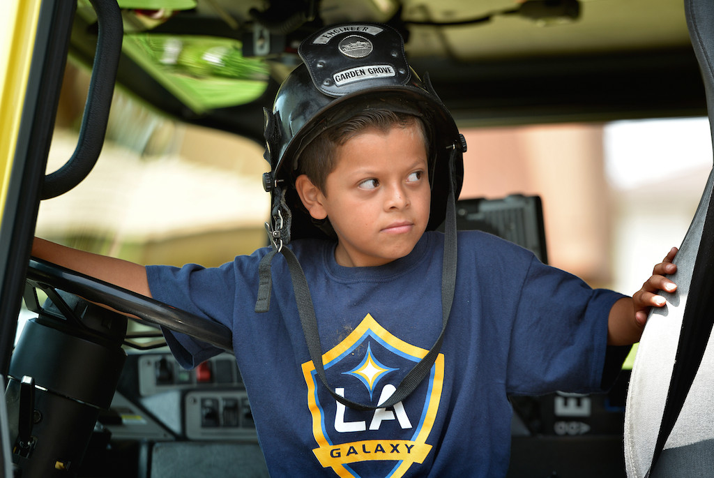Ten-year-old Brian Rayes tries on a firefighter’s engineer hat while sitting behind the wheel of Garden Grove Engine 6 during a community gathering along Laguna Street in Garden Grove. Photo by Steven Georges/Behind the Badge OC