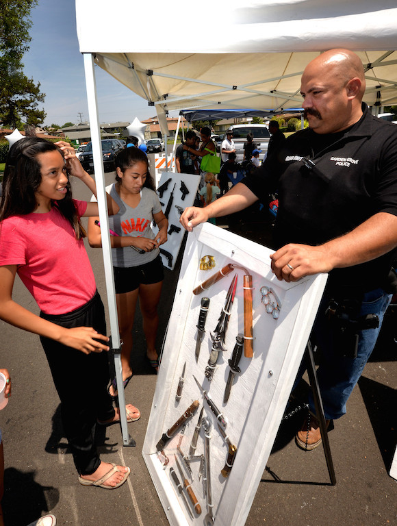 Ashley Marquez, 13, left, talks to Officer Pete Kunkel of the Garden Grove police gang unit about the display of weapons that have been confiscated from gang members in and around the city of Garden Grove. The display was part of a community gathering along Laguna Street in Garden Grove. Photo by Steven Georges/Behind the Badge OC