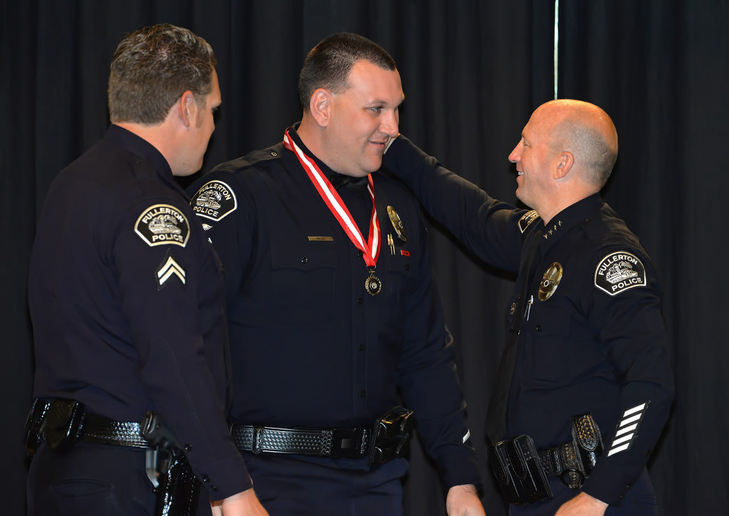 Officer Kyle Baas, center, receives the Medal of Bravery from Chief Dan Hughes during Fullerton PD’s Promotions and Awards Ceremony. Photo by Steven Georges/Behind the Badge OC