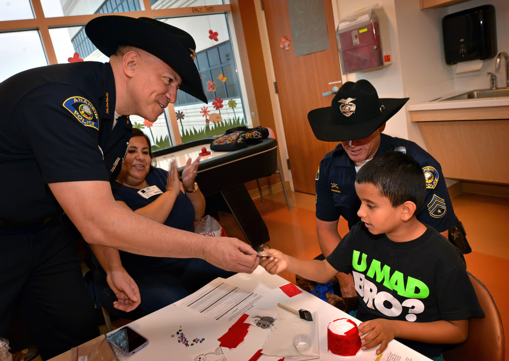 Anaheim Police Chief Raul Quezada, left, hands 9-year-old Cesar Arreola of Long Beach one of his Chief Coins as Sgt. Rodney Duckwitz, behind Cesar, pays him a visit at CHOC hospital. Photo by Steven Georges/Behind the Badge OC
