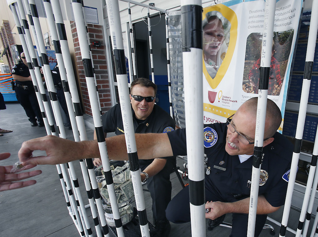 Garden Grove Police Chief Todd Elgin, right, hands out a Garden Grove police department pin while locked into a homemade jail cell with Garden Grove Fire Chief Tom Schultz to collect donations in support of a fundraiser for CHOC-Children’s Hospital of Orange County at the Walmart in Garden Grove.  Photo by Christine Cotter/Behind the Badge OC