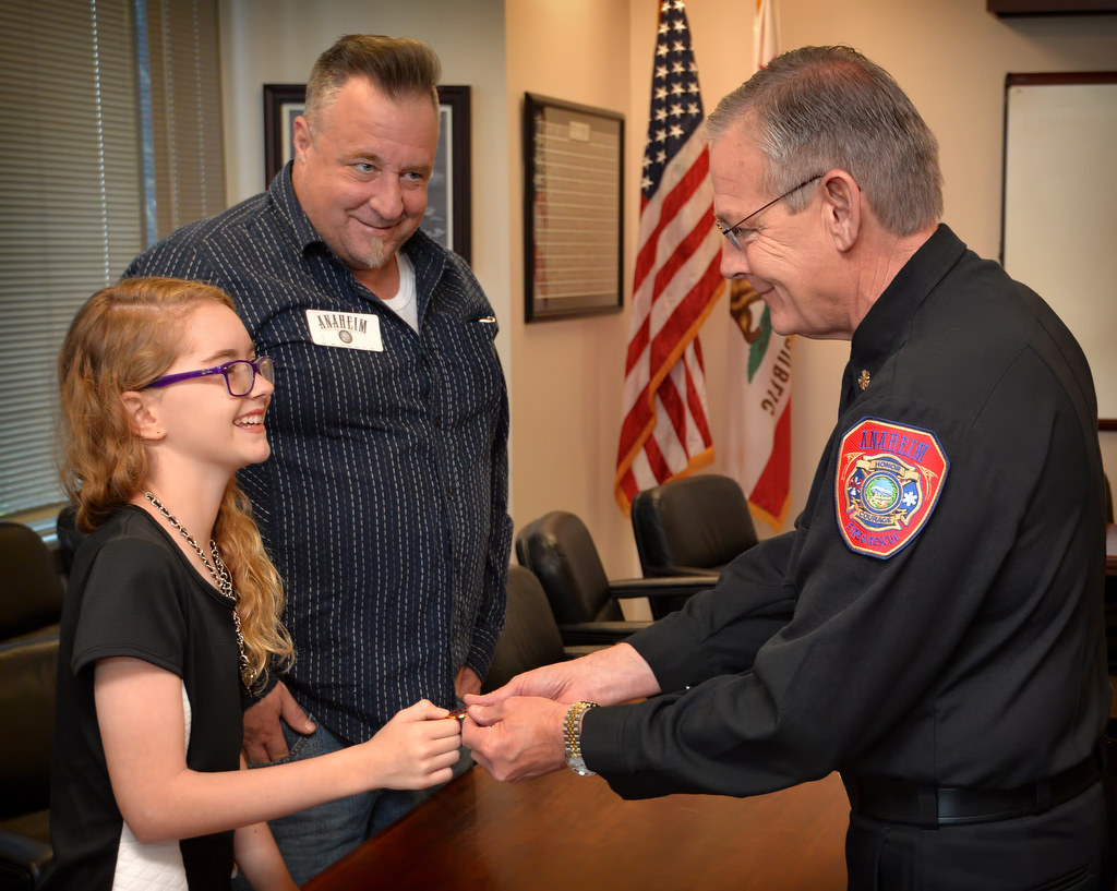 Twelve-year-old Angela Chute receives a ChiefÕs Coin from Anaheim Fire & Rescue Chief Randy Bruegman during a visit to AF&R headquarters to be honored after a 911 call from her helped save William Chute, her father behind her, after he had a seizure. Photo by Steven Georges/Behind the Badge OC