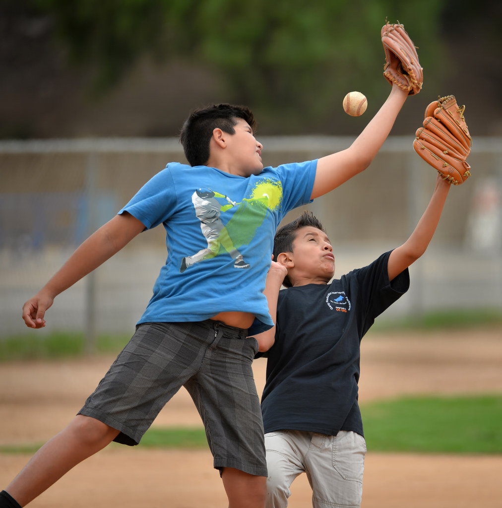 Alejandro Avila, left, and Humberto Ferrusca, both 12, leap for the ball during a baseball camp for at-risk kids at "The YardÓ in Fullerton. Photo by Steven Georges/Behind the Badge OC
