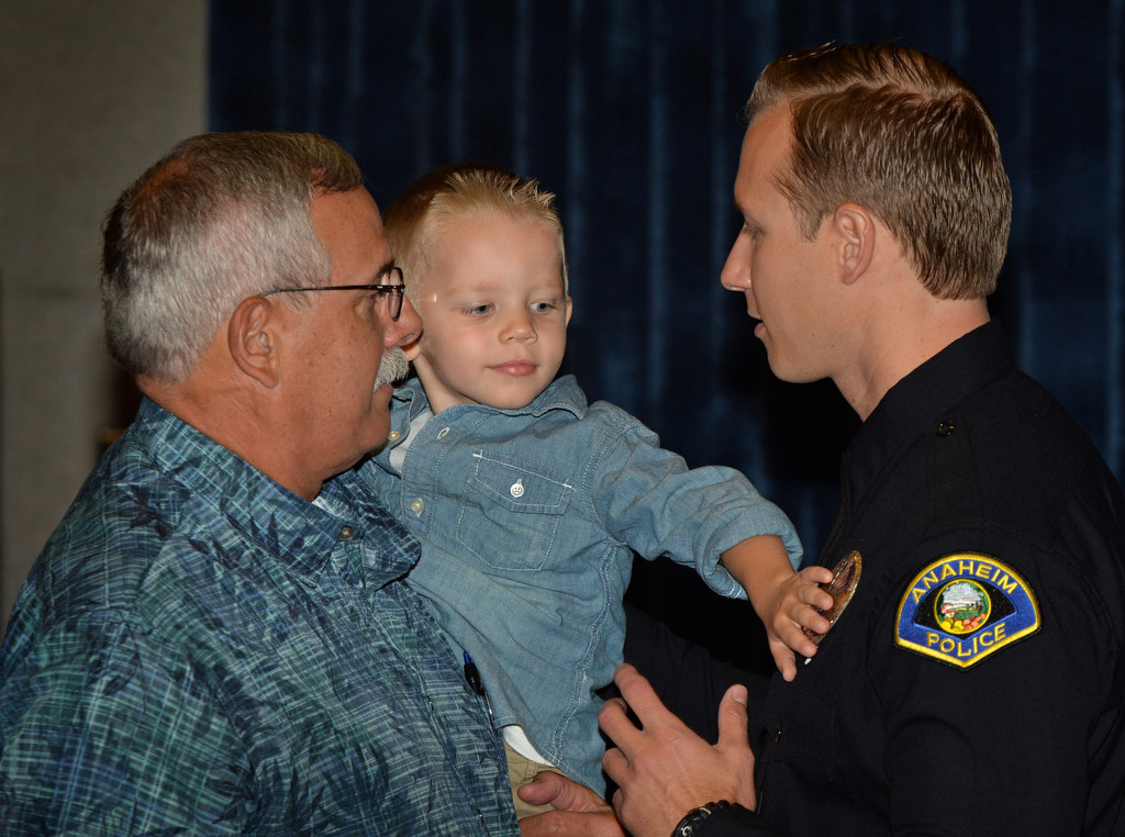 Three-year-old Kaden places his hand on his father’s new Anaheim PD officers badge after Kurt Lockwood receives the new badge during a promotional ceremony as Kurt’s father Ken, left, stands on stage with him. Lockwood comes from the Los Angeles PD. Photo by Steven Georges/Behind the Badge OC