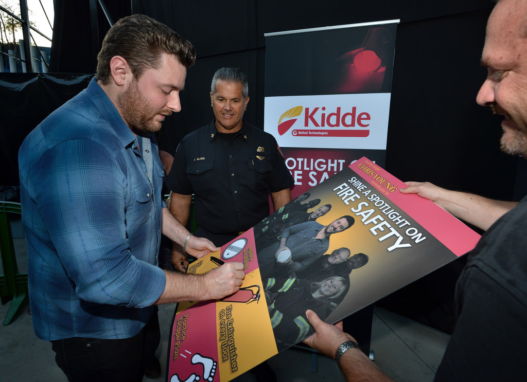 Country singer Chris Young signs a poster on fire safety featuring him with Anaheim Fire & Recue Deputy Chief Jeff Alario behind him and Neal Zipser of Kidde Fire Safety, right, holding the poster. Photo by Steven Georges/Behind the Badge OC