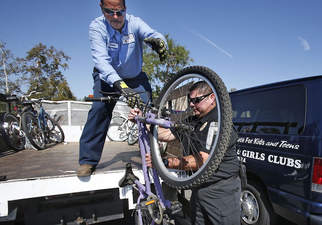 La Habra Parks Department employee Pablo Pabon, top, hands a child's bicycle to La Habra Police Department's Senior Property and Evidence officer Jessie Jaime. The lost and stolen bicycles were given to the Boys & Girls Club during their summer program. Photo by Christine Cotter/Behind the Badge OC