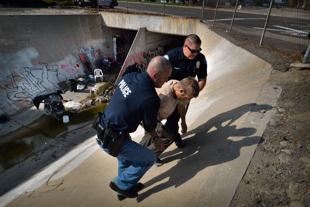 A Garden Grove PD officers helps a homeless man living in a flood canal under Western Ave. up the steep embankment as the Garden Grove Homeless Task Force conducts a cleanup sweep. Photo by Steven Georges/Behind the Badge OC