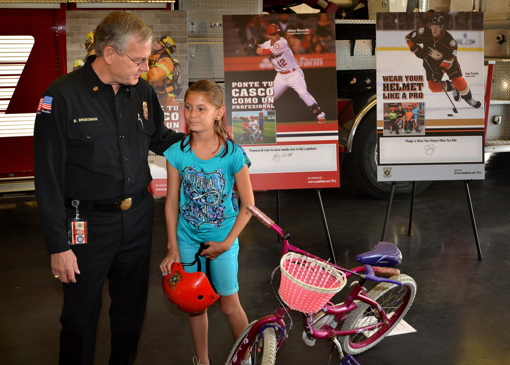 Anaheim Fire & Rescue Chief Randy Bruegman with 10-year-old Morgen Alvarez of Anaheim during a press conference on bicycle helmet safety and the campaign called Wear Your Helmet Like A Pro that includes the design of the safety posters behind them. Photo by Steven Georges/Behind the Badge OC