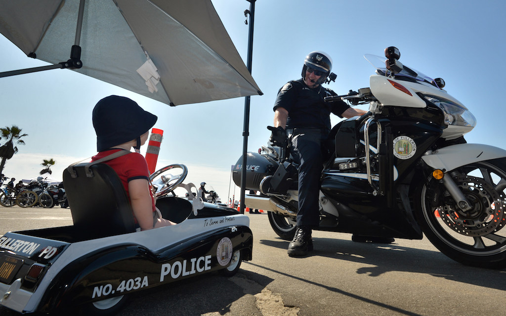John William Baas, left, watches his father, Fullerton Officer Kyle Baas, get ready for the OCTOA competition as John sits in his pedal police car.  Photo by Steven Georges/Behind the Badge OC