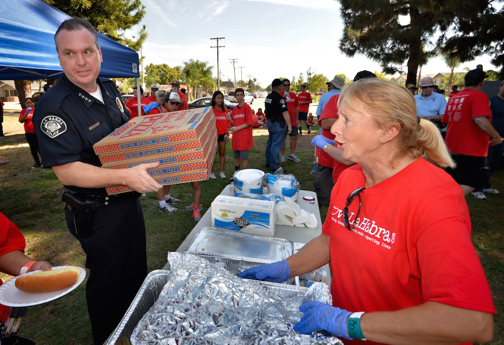 La Habra Police Chief Jerry Price brings boxes of pizza donated by Jane and Steve Williams (Jane use to run the La Habra Journal) to the table for the Love La Habra volunteers as Reini Weyant right, gets the hot dogs ready. Photo by Steven Georges/Behind the Badge OC