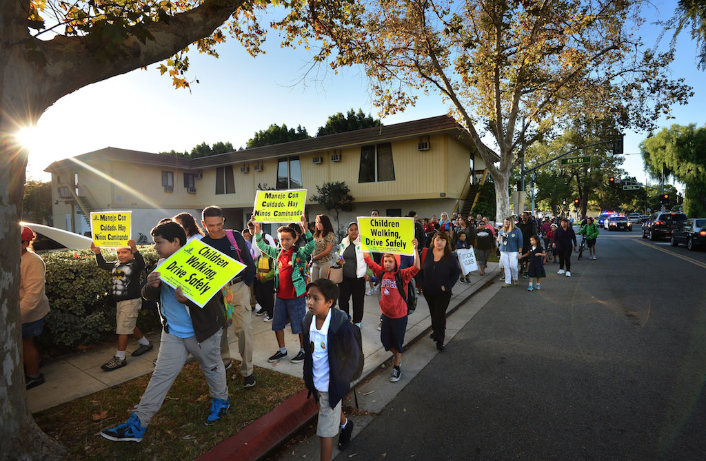 Holding safety signs in English and Spanish saying “Children Working, Drive Safely,” kids walk up North B Street to Estock Elementary School during Tustin PD’s annual Walk to School. Photo by Steven Georges/Behind the Badge OC