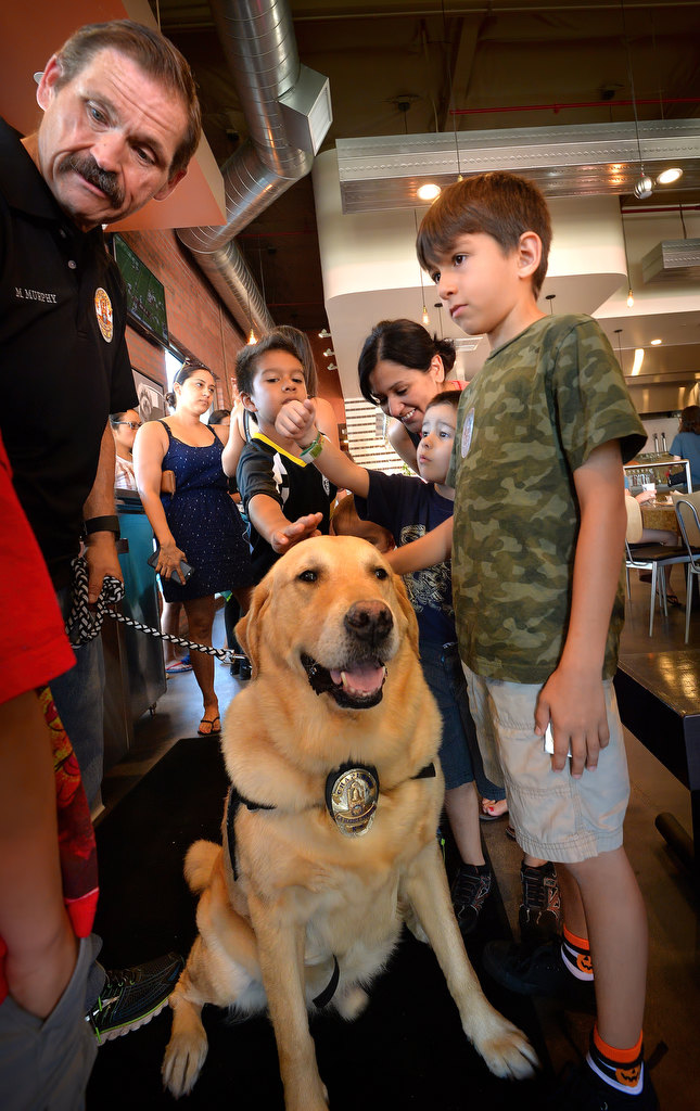 La Habra PD Chaplain Mike Murphy, left, keeps an eye on Emerson, a crisis K-9 with the La Habra PD, during the Pizza with a Police Pup event as kids gather around to reach in and pet the police dog that has helped many people cope during difficult times. Photo by Steven Georges/Behind the Badge OC