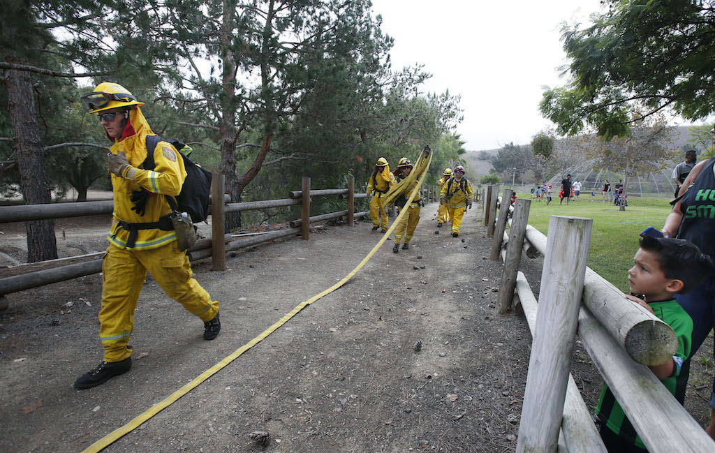 Fire fighters haul hoses up a dirt trail during a demonstration of progressive hose laying at the Ready, Set Go Block Party.   Photo by Christine Cotter/Behind the Badge OC
