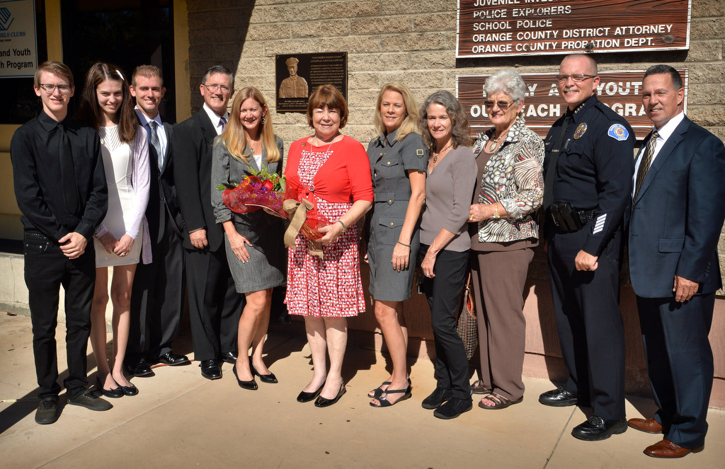 Lollie Beauchamp, center with flowers, stands with her family, Chief Todd Elgin, and former GGPD Chief Kevin, right, in front of a plaque of her late husband, GGPDÕs Sgt. Bruce Beauchamp, during a naming ceremony for the Bruce Beauchamp Juvenile Justice Center. Photo by Steven Georges/Behind the Badge OC
