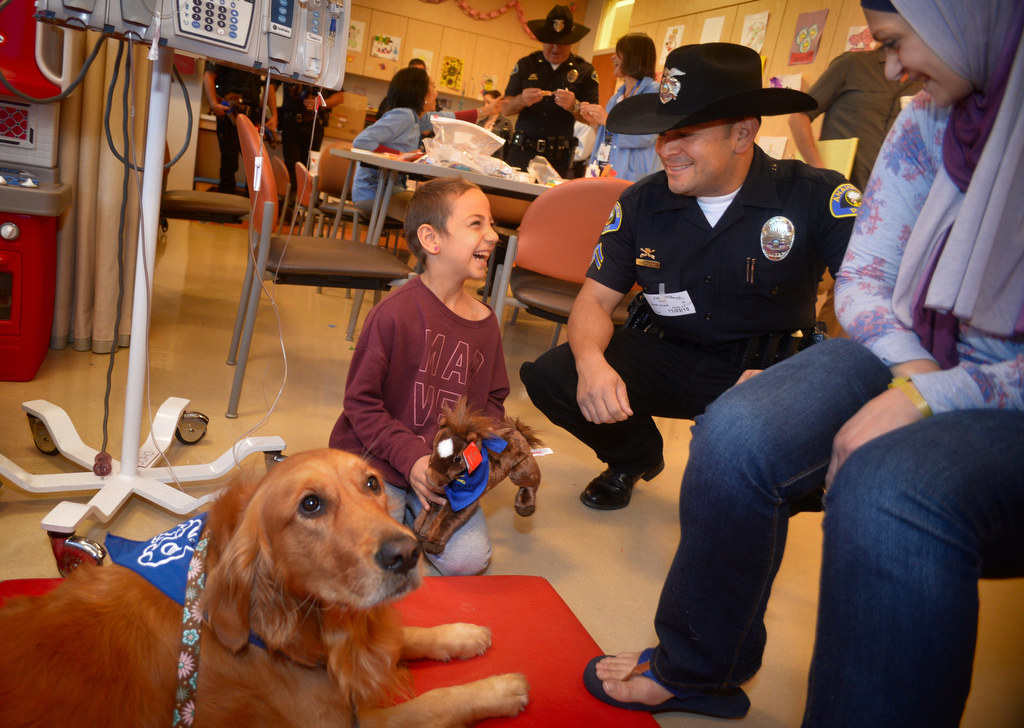 Seven-year-old Maria Suleiman of Anaheim shares a laugh at CHOC Hospital with Anaheim PD Officer Tinajero during a visit with Maria, her mother Gamela Alawneh, right, and Spice, a CHOC therapy dog. Photo by Steven Georges/Behind the Badge OC