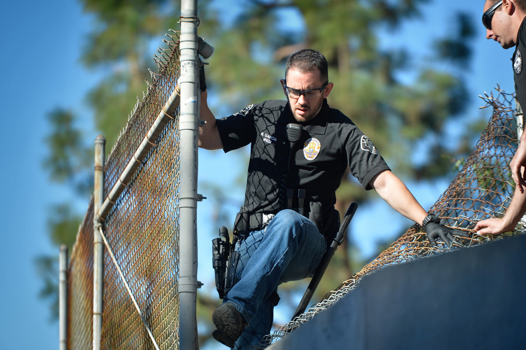 La Habra PD Officer Nate Garcia climbs through a cut chain linked fence as a task force from La Habra and Fullerton PD look for living around the flood control channels. Photo by Steven Georges/Behind the Badge OC