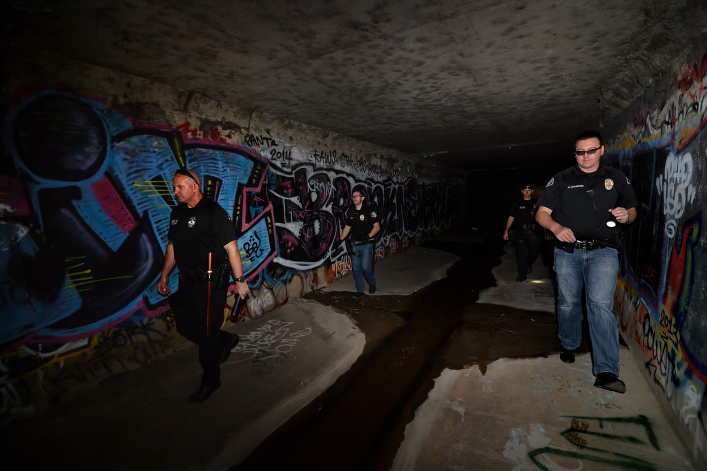 Fullerton PD Cpl. Dan Heying, left, La Habra PD Officer Nate Garcia, Fullerton PD Officer Brad Fernandes and La Habra PD Officer Muris Lucarevic walk through dark flood control tunnel looking for homeless people that might be living in there. Photo by Steven Georges/Behind the Badge OC