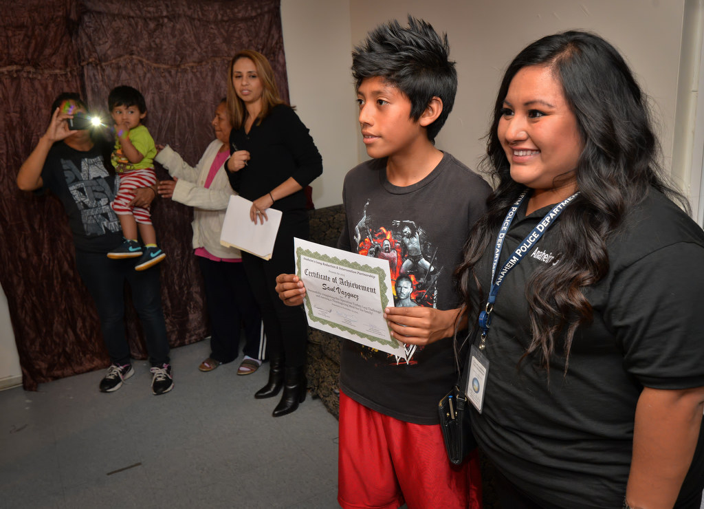 Saul Vazquez, 12, stands next to Carmela Mendoza, case manager for Anaheim PD’s GRIP program after receiving a certificate and a Thanksgiving meal delivered to his home. Photo by Steven Georges/Behind the Badge OC