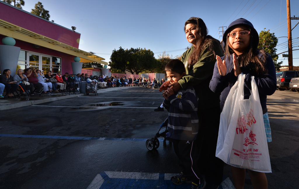 Blanca Lopez of Tustin and her two kids Jared Guerrero, 4, and Jacqueline Guerrero, 8, join the rest of the line in applauding the Tustin Police as they get ready to hand out free turkeys for those in need the day before Thanksgiving. Photo by Steven Georges/Behind the Badge OC