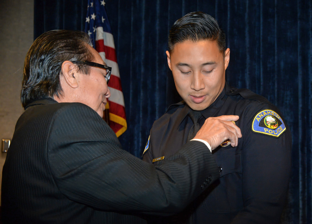 Anaheim PD’s new officer, Phillippe Huynh, has his new badge pinned to him by his father, Allan Huynh, during a promotion ceremony. Photo by Steven Georges/Behind the Badge OC