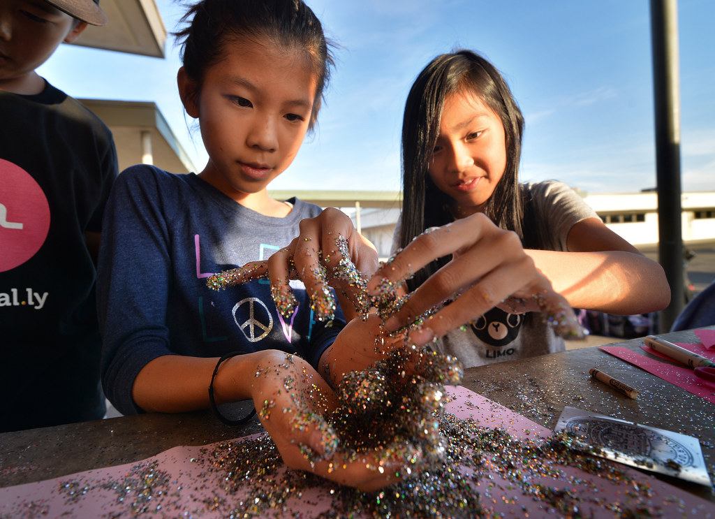 Hellen Nguyen, left, and Vivian Le, both 10, apply lots of glitter, and glue, to part of a decoration (not a cookie) for the Garden Grove PD. Photo by Steven Georges/Behind the Badge OC