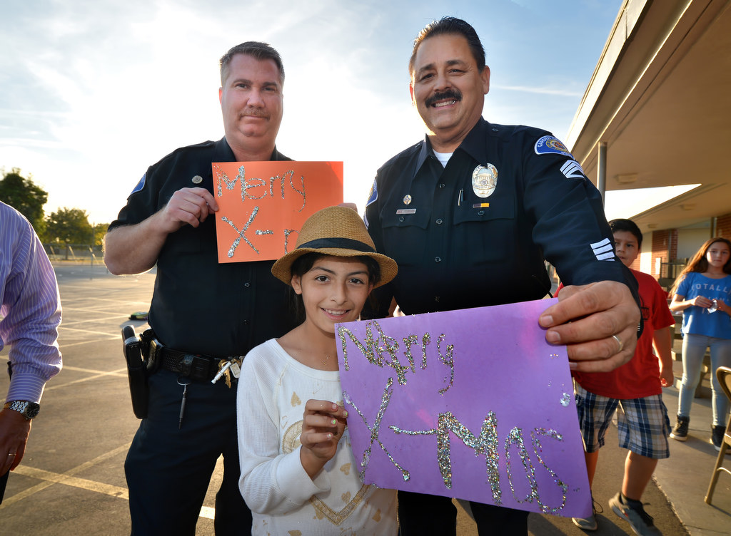 Nine-year-old Aaliyah Valencia of Post Elementary School, presents Garden Grove Officer Andy Flaws, left, and Sgt. John Reynolds with Merry Christmas Cards made of glitter during a visit by the officers. Photo by Steven Georges/Behind the Badge OC